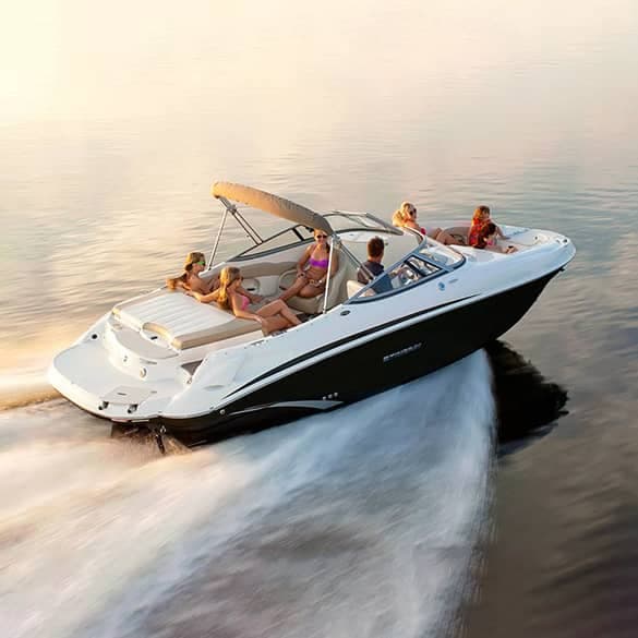 A blue and white motorboat with two people on board cruising on a calm body of water. The boat has fishing rods mounted on the back, and the passengers appear to be enjoying the ride.